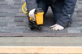 Workman using pneumatic nail gun install tile on roof of new house under construction