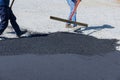 Workmen working on the pavement of a road are laying asphalt while shoveling black gravel, preparing it for the paving