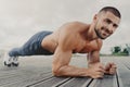 Workout and healthy lifestyle concept. Pleased muscular bearded young man stands in plank pose, makes sport training outdoors,