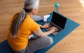 Workout at home, health care and sports blog. Senior woman typing on laptop with empty screen, sitting on yoga mat Royalty Free Stock Photo