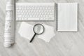 Workplace with architectural drawings, keyboard, magnifier and notepad in top view.