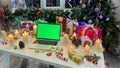 Workplace decorated for the New Year. An open laptop with a chroma key on the screen lies on a white wooden table. Christmas gifts