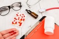 Workplace of doctor. Pills in hand, red stethoscope, clipboard and glasses on white wooden table