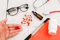 Workplace of doctor. Pills in hand, red stethoscope, clipboard and glasses on white wooden table Royalty Free Stock Photo