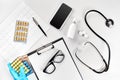 Workplace of a doctor. Pills in hand, stethoscope, clipboard and glasses on white table