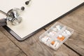 Workplace of a doctor. Stethoscope, clipboard, pills and other stuff on wooden desk Royalty Free Stock Photo