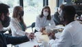 Workplace with epidemic safety measures. Young multiethnic business colleagues work at office table meeting, wear masks.