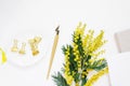 Workplace of a female calligrapher. Pen, yellow mimosa flowers, paper clips on a saucer and notebooks on a white background