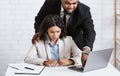 Workplace harassment. Boss touching his young attractive female assistant while she working on laptop at office Royalty Free Stock Photo