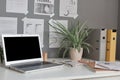 Workplace at home or in office with table, laptop with empty display, flower, paper folders, notes on wall