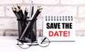 A workplace in the house with glasses, pencils in a stand and a notebook with text SAVE THE DATE on a brick wall background. Home Royalty Free Stock Photo