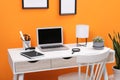 Workplace with laptop, stationery on desk and chair near orange wall. Home office Royalty Free Stock Photo