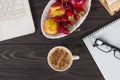 Workplace mockup with a cup of cappuccino coffee and fresh fruits on a wooden dark table with a laptop and notepad Royalty Free Stock Photo