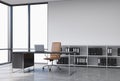 A workplace in a modern corner panoramic office with copy space in the windows. A black desk with a laptop, brown leather chair an