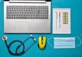 Workplace of a modern doctor. Laptop, wireless mouse, notebook, stethoscope, pills on a blue background. Top view, minimalist