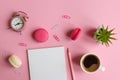 Workplace with notepad, pencil, alarm clock, plant, a cup of coffee and macarons on a pink background. Business
