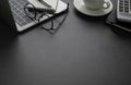 Workplace office with dark grey desk. Close-up view from above of laptop, glasses with notebook and cup coffee. Tabletop space for