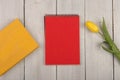 Yellow flower tulip, blank red notepad and book on a white wooden table
