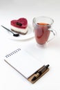 Workplace of a romantic girl. An open notebook, a cup of tea and a heart-shaped homemade cheesecake Royalty Free Stock Photo