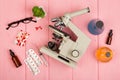 Workplace scientist doctor - microscope, pills, syringe, eyeglasses, chemical flasks with liquid on pink wooden table Royalty Free Stock Photo