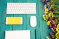 Workplace with wireless slim keyboard, mouse, smart phone, notepad, pencil, colorful flowers on blue wooden desk