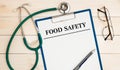 Worksheet with the inscription Food Safety, stethoscope, glasses, pen