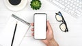 A men's hand holds a smartphone with a white screen on the background of the workplace Royalty Free Stock Photo