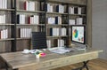 Workspace with desktop computer on wooden desk and black chair with bookshelf on the background