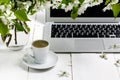 Workspace with girl`s hand on laptop keyboard and cup of coffee, white spring apple tree flowers on white woodden background. Vie Royalty Free Stock Photo