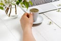 Workspace with girl`s hand on laptop keyboard and cup of coffee, white spring apple tree flowers on white woodden background. Vie Royalty Free Stock Photo