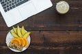 Workspace with laptop and with a healthy breakfast: mango, orange and muesli bar on wooden table. Copy space, top view