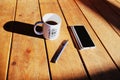 Workspace outside with white mug with coffee with a cellphone and a pen on a sunny day