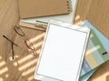 A workspace setup with a tablet, notebooks, glasses, and stationery on a wooden table illuminated by soft sunlight Royalty Free Stock Photo