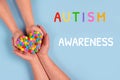 World Autism Awareness Day concept - autistic child`s hands supported by mother holding multicolored heart on blue background.