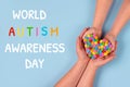 World Autism Awareness Day concept - autistic child`s hands supported by mother holding multicolored heart on blue background.