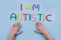 World Autism Awareness Day concept - multicolored letters, Am I Autistic - child hands playing against blue background