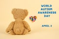 World Autism Awareness Day concept - sad teddy bear and multicolored defocused heart against yellow background. Autism spectrum