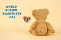 World Autism Awareness Day concept - sad teddy bear and multicolored defocused heart against yellow background. Autism spectrum