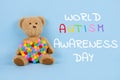 World Autism Awareness Day concept - sad teddy bear with multicolored heart sitting against blue background. Autism