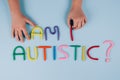 World Autism Awareness Day concept, symptoms - multicolored letters, Am I Autistic - on light blue background with child hand.