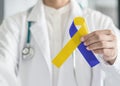 World down syndrome day blue yellow awareness ribbon on doctor`s hand for raising support on patient with down syndrome illness