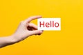 World greeting day. A woman`s hand holds a business card with the text Hello. Close up. Yellow background Royalty Free Stock Photo