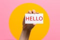 World hello day. Raised female hand with a card with the inscription Hello. Pink background with a yellow circle Royalty Free Stock Photo