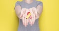 World Hepatitis Day concept. Girl in gray T-shirt holds in her hands awareness symbol red-yellow ribbon. Yellow background Royalty Free Stock Photo