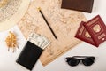 World map, pencil, two passports, sunglasses, shell, black wallet with money and a straw hat on a white wooden table