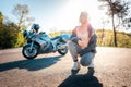 World Motorcyclist Day. A young woman with tattoos on her arm, wearing leather jacket, and posing sitting. Road and