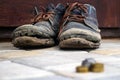 Worn boots with a lagging sole on a background of gray pavers and dark brown wood. In the foreground is a blurred stack of coins.