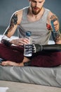 Worn out cyborg man with bionic hand sitting on a mat, opening water bottle