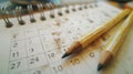 Worn pencils on a stained paper calendar, symbolizing heavy scheduling, planning