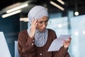 A worried Arab woman in a hijab sits in the office and holds a letter, a document in her hands Royalty Free Stock Photo